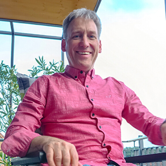 Lachender Mann in pinkem Hemd sitzt auf einem Bürostuhl