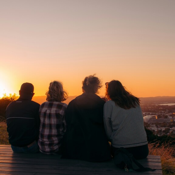 Vier Menschen sitzen nebeneinander und gucken auf den Sonnenuntergang über der Stadt